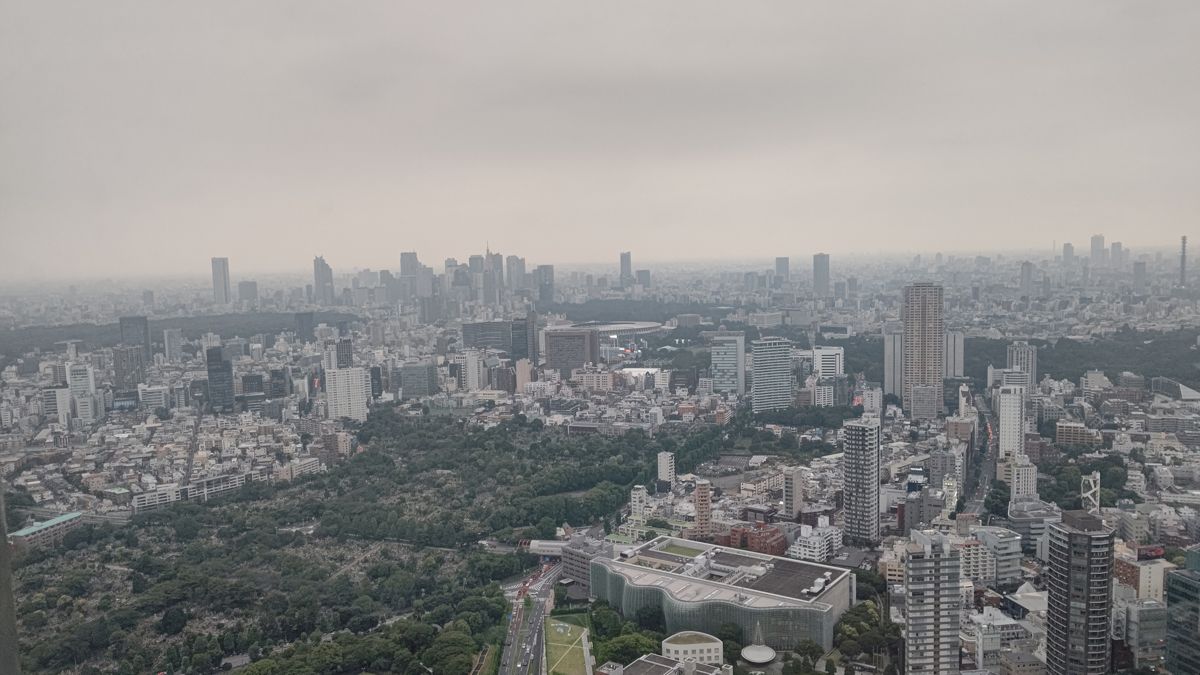 曇り空の下、六本木の高層階から見た都心。手前に青山霊園の緑、中ほどに国立競技場と外苑の森、遠くに新宿の高層ビル群