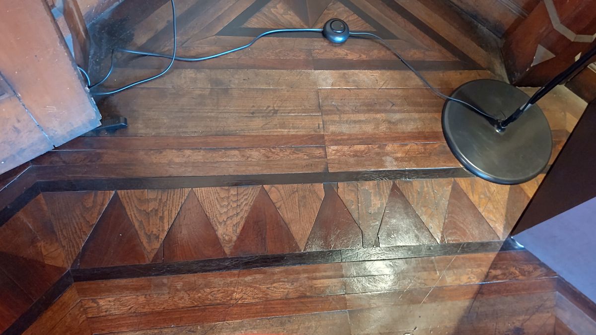 濃い色と淡い色の木を三角形に組み合わせた寄木の床。部屋の縁に沿って模様が続く