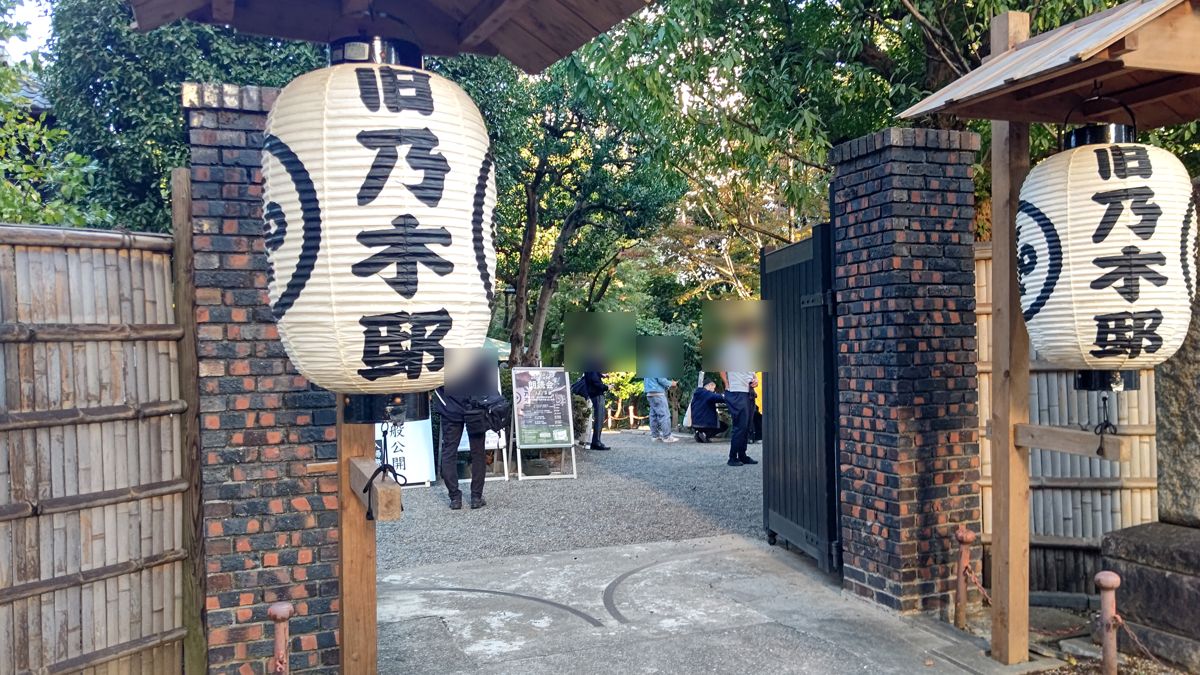 れんがの門柱に「旧乃木邸」と書いた提灯が下がり、開いた木の門扉の奥に砂利の庭と木々が見える
