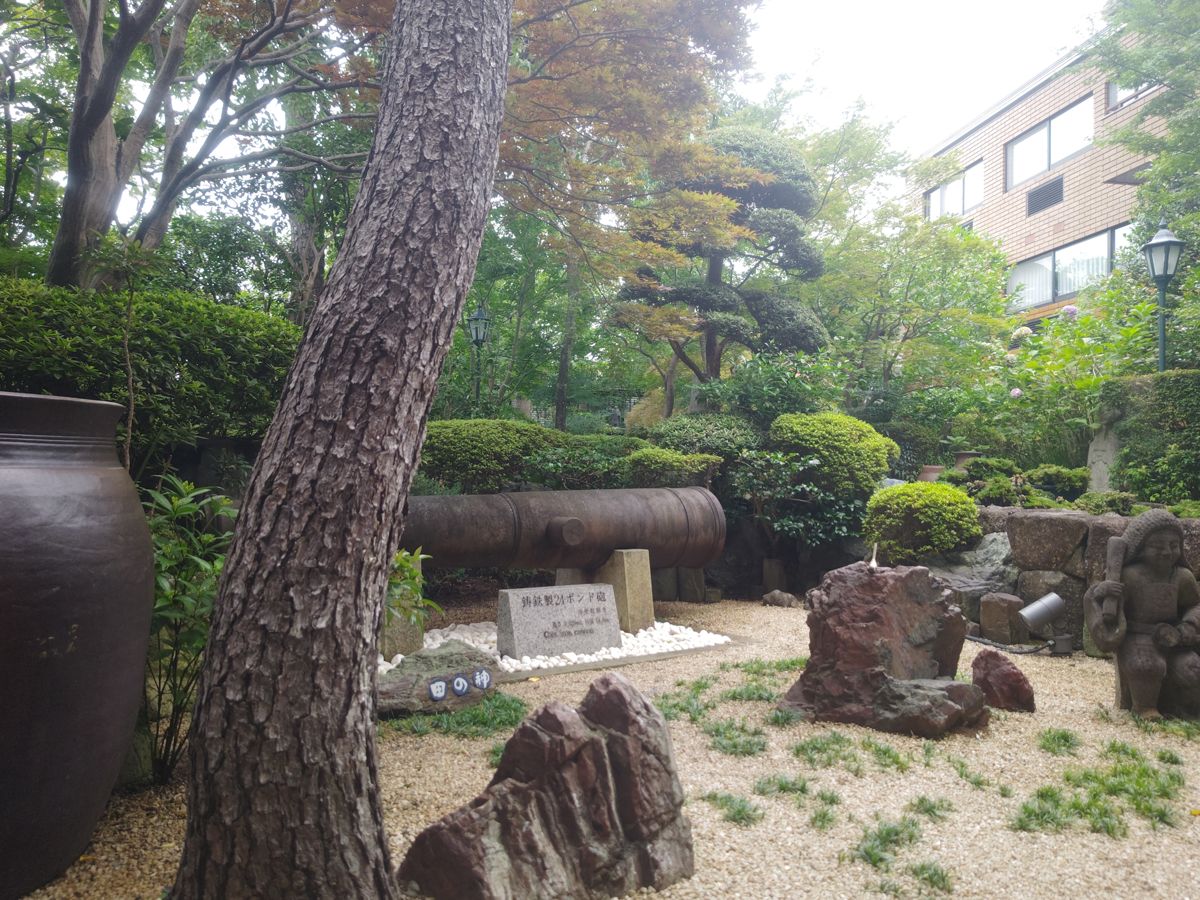 マツの幹と刈り込んだ植え込み、白い砂利に据えた岩や石像、大きな壺が並ぶ庭